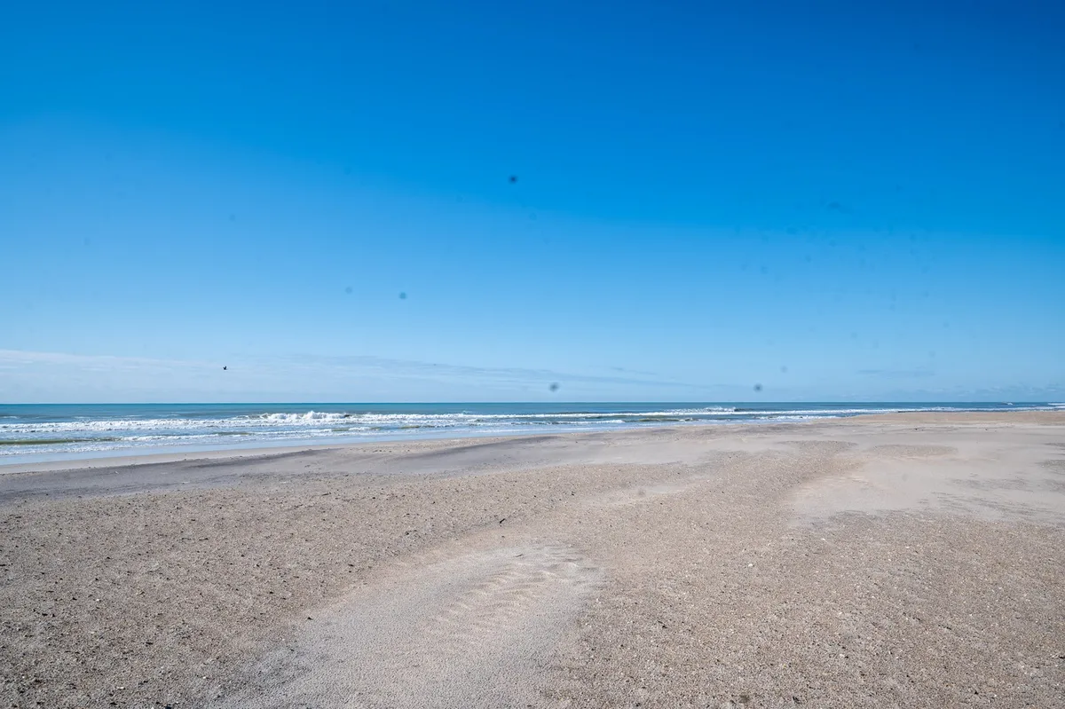 A wide stretch of soft sandy beach bordered by gentle waves under a clear blue sky, capturing the peaceful and inviting shoreline of North Topsail Beach. The absence of crowds emphasizes the tranquility and natural beauty of the area.