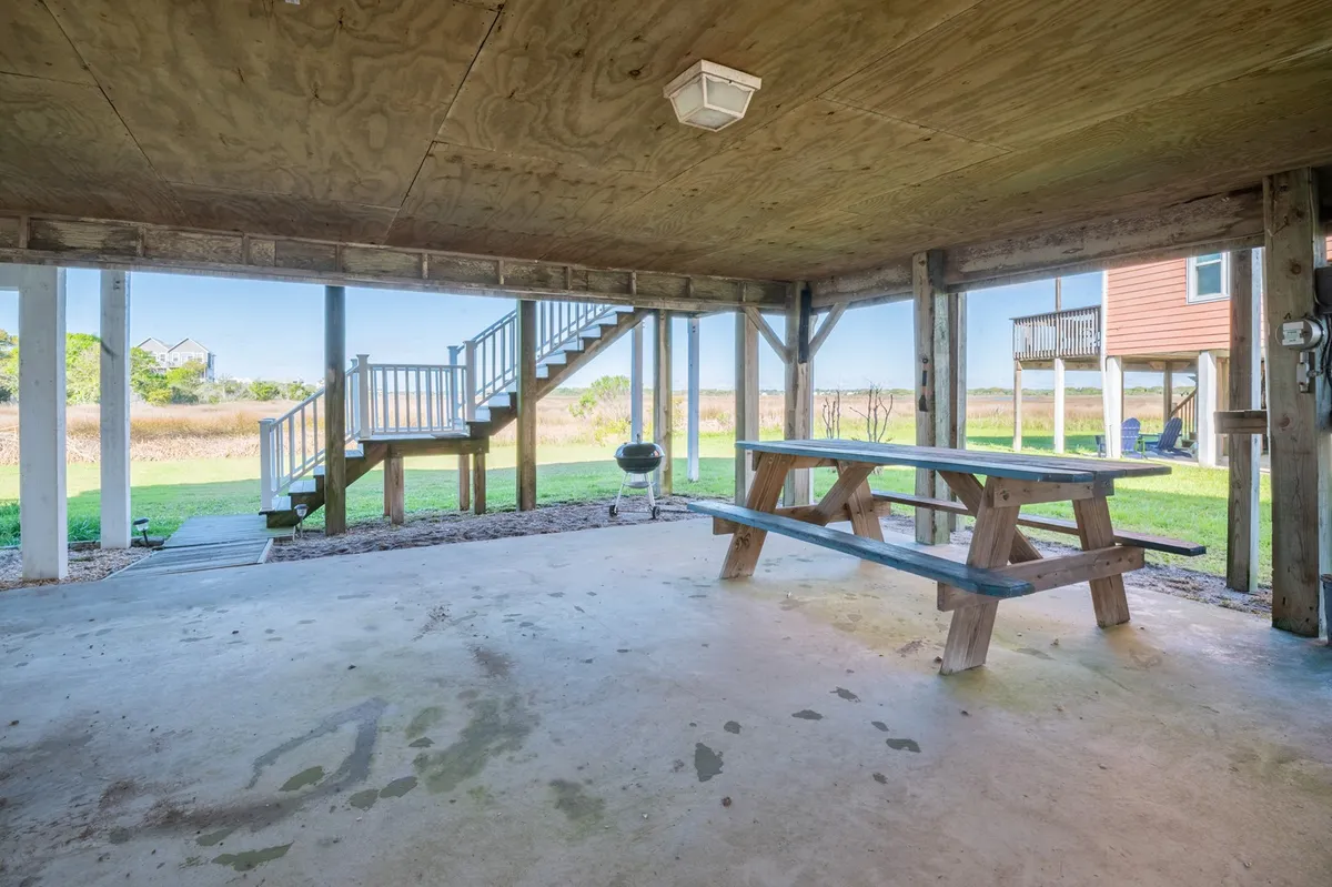 This image captures a casual, welcoming ground-level space featuring a picnic table, a visible staircase, and a grill, all set for family gatherings or cookouts in the shade beneath the house.
