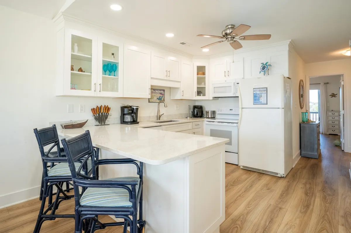 A modern kitchen featuring white cabinetry, a central island with seating (breakfast bar), and stainless steel appliances. The space is designed for both cooking and socializing, with plenty of counter space and a layout that encourages shared meal preparation and conversations.