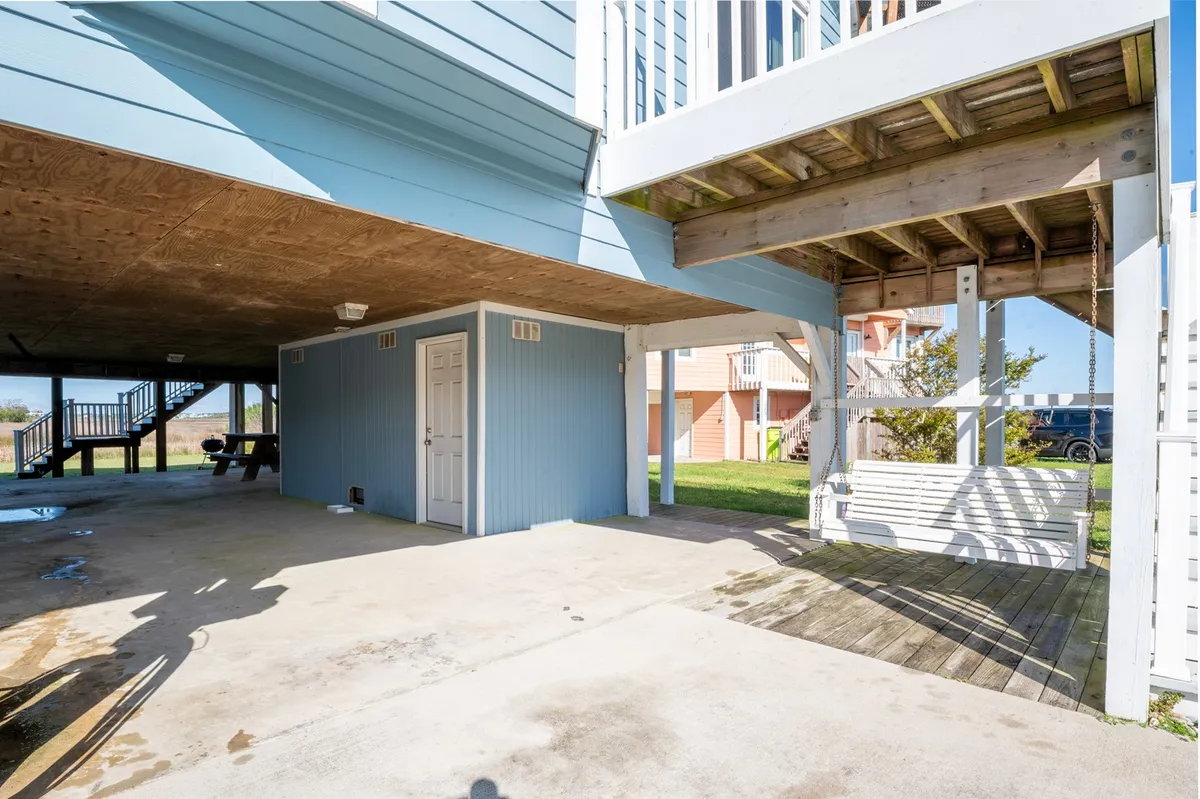 A bright, inviting exterior shot focusing on the white swing bench against a blue exterior wall, atop a concrete surface, evoking moments of relaxation and casual gatherings.