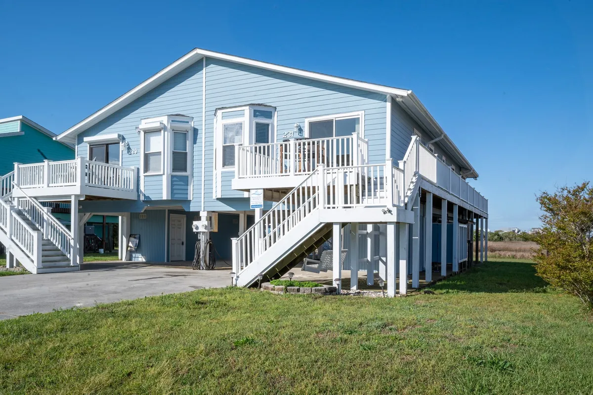 The exterior of a charming blue single-family house is showcased, featuring crisp white railings and stairs leading up to a spacious porch. The lush green lawn surrounding the home invites relaxation and outdoor gatherings. The porch promises beautiful sunset views and a perfect spot for morning coffee or evening stargazing.